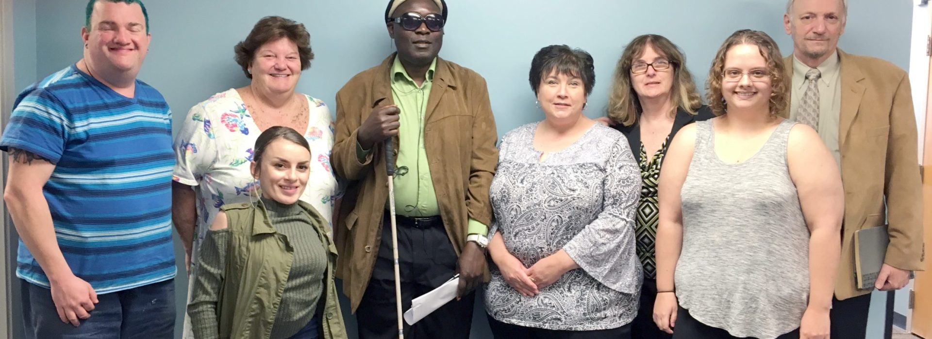 A group of standing smiling adults with and without disabilities.