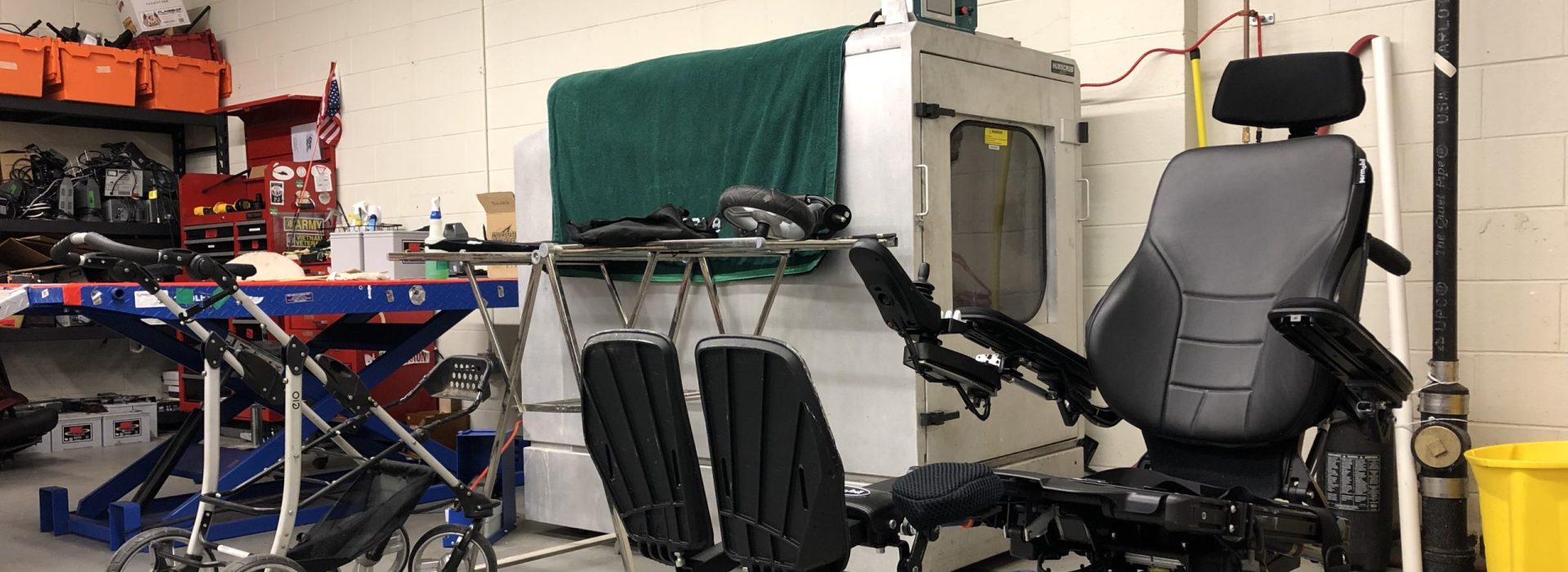 Reclined power wheelchair chair with hubscrub machine behind and other items of durable medical equipment. 