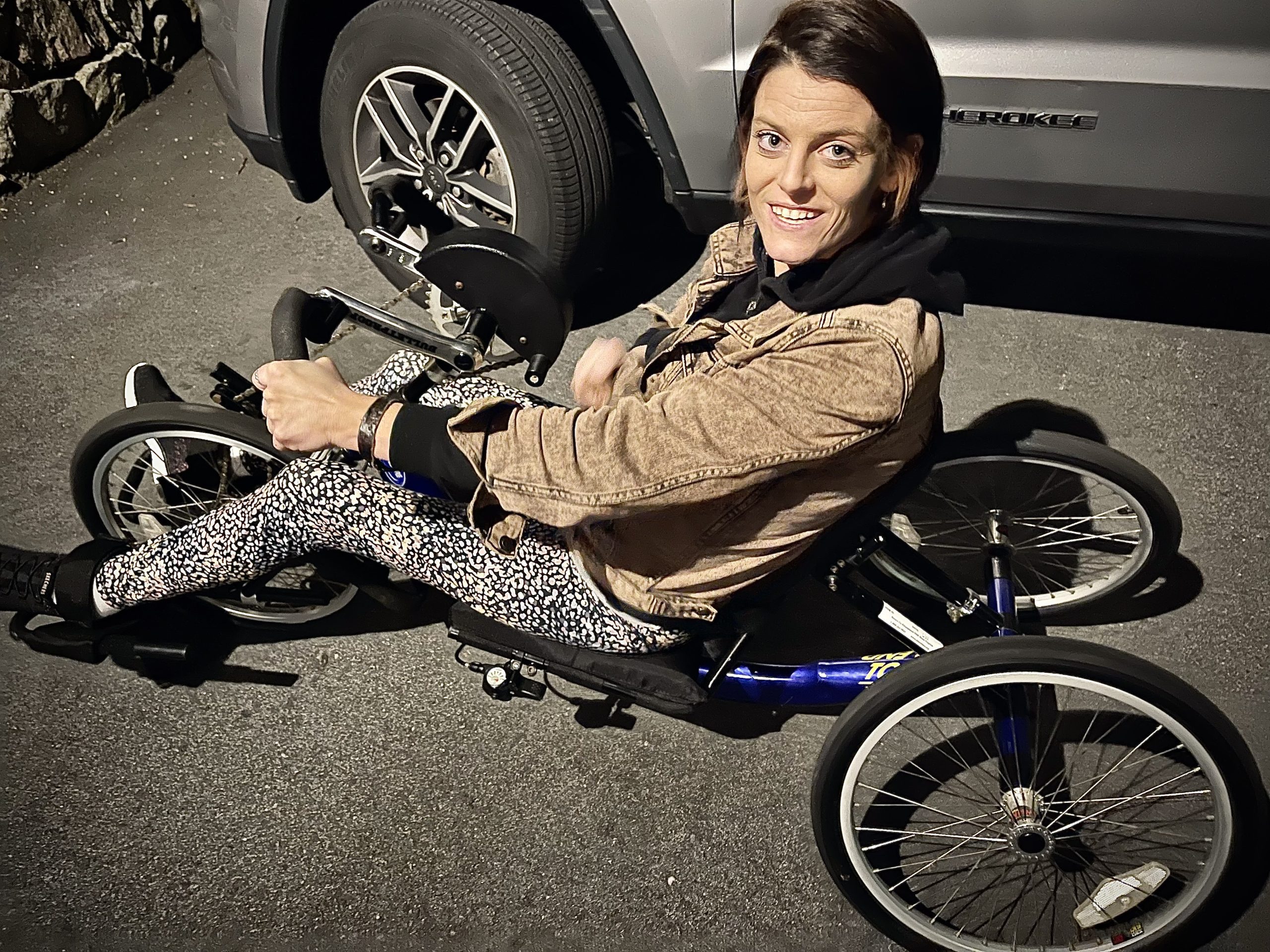 A woman smiles seated in a handcycle trike.