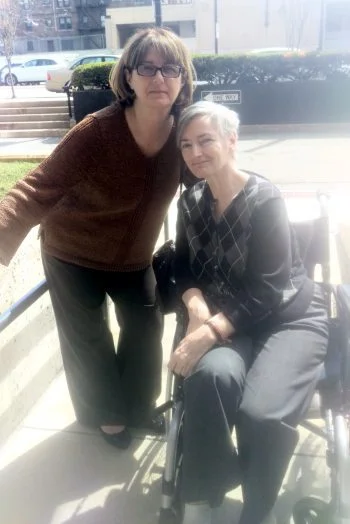Two women, one standing and one seated in a manual wheelchair